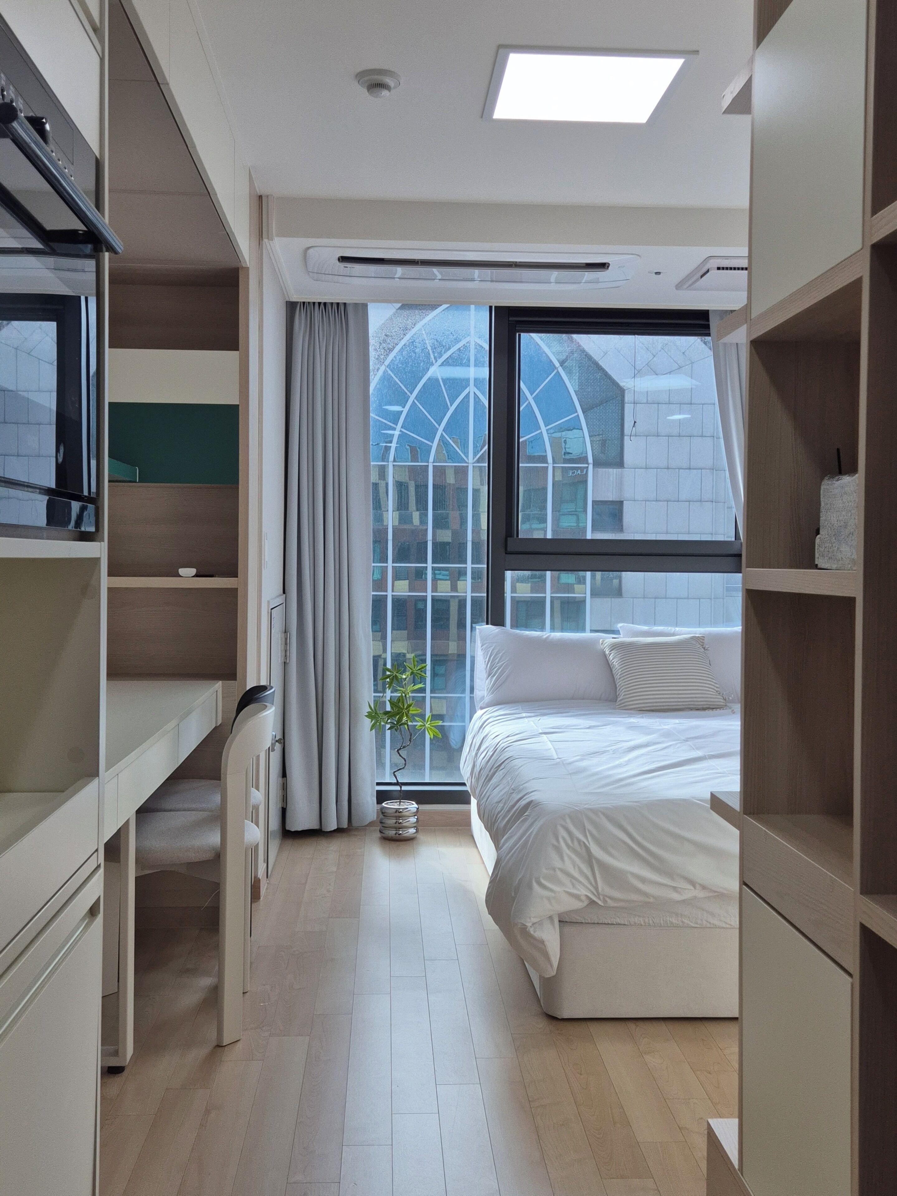 A modern hotel room with a bed, built-in wardrobe, and a large window with a view of a building.