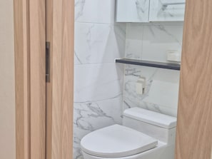 Ein Badezimmer mit Toilette, einer Wand mit Marmorplatten und einer Holztür.