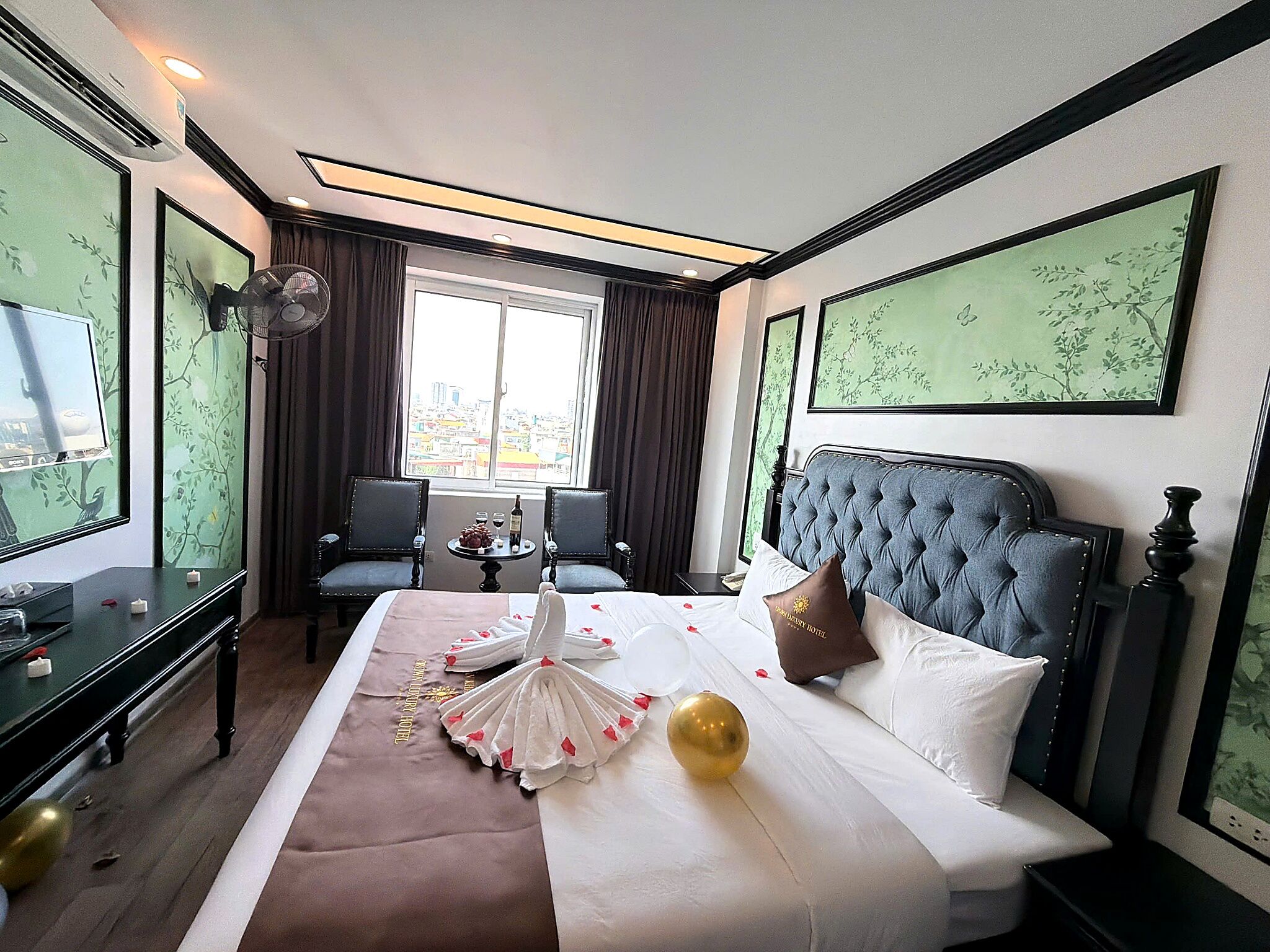 A hotel room with a large bed, a sitting area with two chairs, a small table, and a window with a city view.