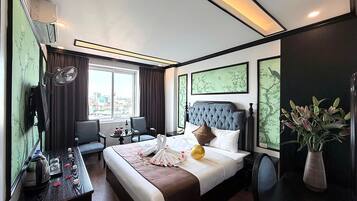 Una habitación de hotel con una cama grande, una zona de estar con una mesa y sillas, vistas de la ciudad a través de la ventana y obras de arte en las paredes.