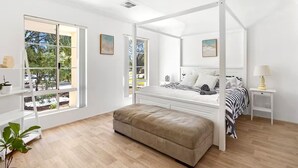 A spacious bedroom with a four-poster bed, large windows, a wooden floor, and a small bedside table. - Avalon Beach Escape| Coastal Retreat -5 minutes to beach, Spa, Sauna & Sleeps 11 (Wannanup)