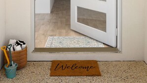 A white door with glass panels, a welcome mat, and a small basket with cleaning tools. - Avalon Beach Escape| Coastal Retreat -5 minutes to beach, Spa, Sauna & Sleeps 11 (Wannanup)
