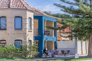 Ein Gebäude mit blauer Fassade, einem Balkon mit Schild und Außenbestuhlung.