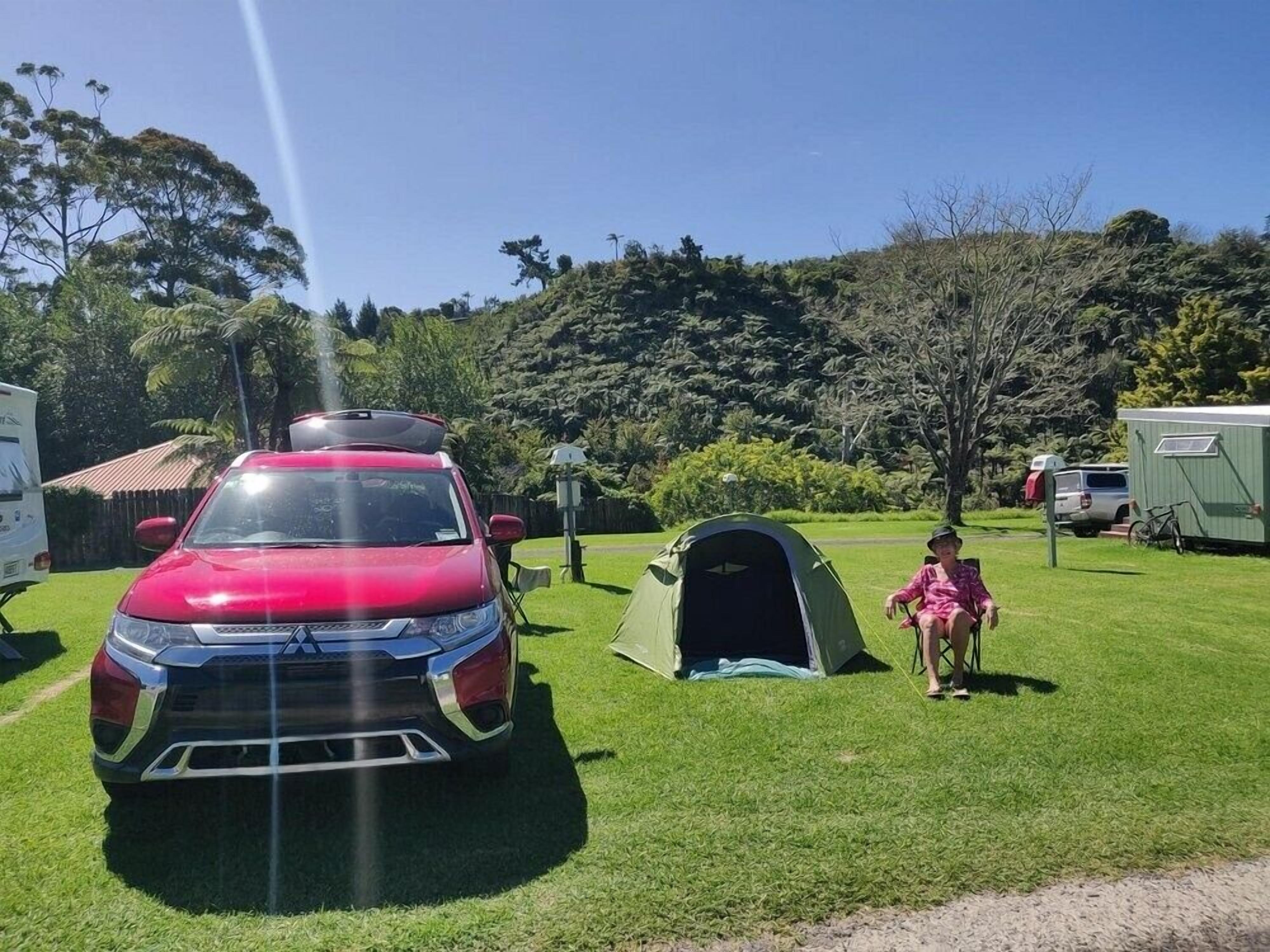 Ein rotes Fahrzeug auf einer Wiese mit einem Zelt und einer Person in einem pinkfarbenen Outfit.