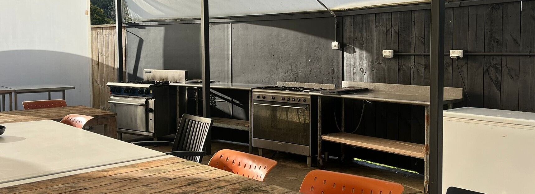 A kitchen with a stove, oven, and sink, wooden chairs, and a table.