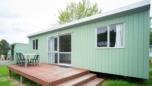 Una casa móvil verde con un porche de madera y una mesa con sillas.