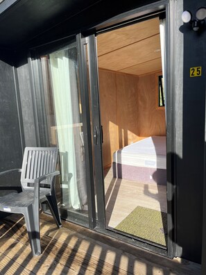 A room with a bed, a chair, and a sliding glass door leading to an outdoor area. - Welcome Bay Hot Pools and Accommodation (Tauranga)