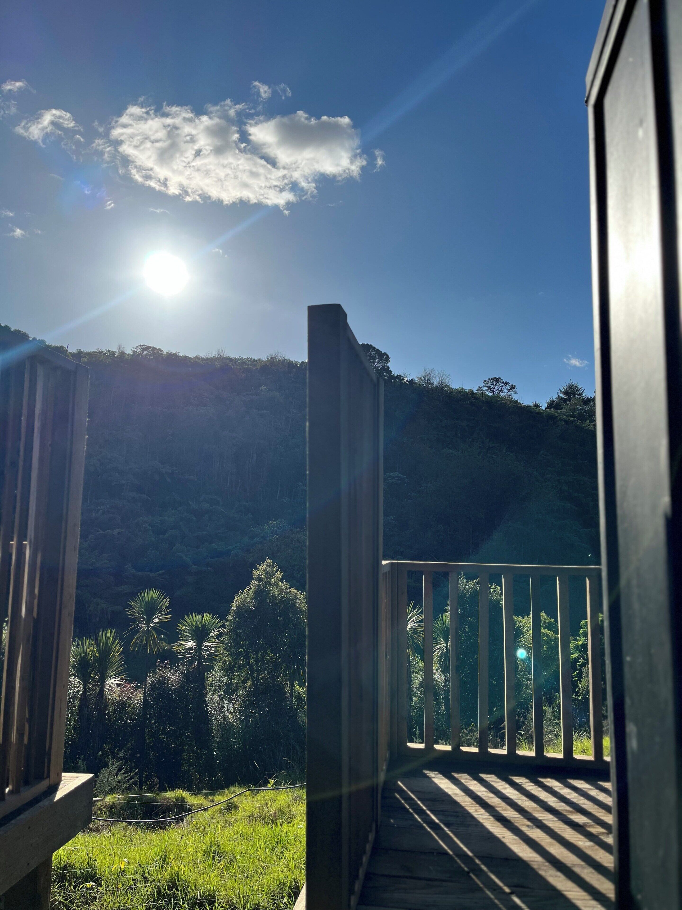 Un balcon offrant une vue sur une colline boisée, un ciel dégagé et un soleil éclatant.