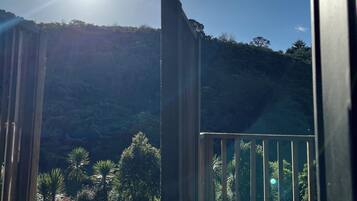 A balcony with a view of a forested hillside, a clear sky, and the sun shining.