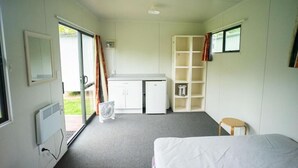 Una habitación con cama, escritorio, silla, ventilador y una pequeña mesa.