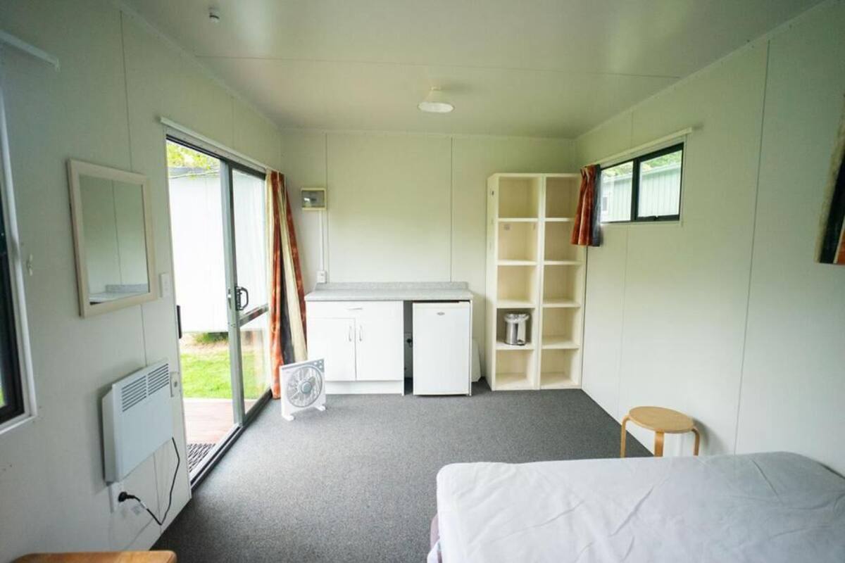 Una habitación con cama, escritorio, silla, ventilador y una pequeña mesa.