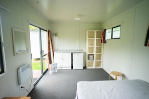 Una habitación con cama, escritorio, silla, ventilador y una pequeña mesa.