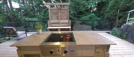 Una cocina exterior con una parrilla empotrada, una mesa de madera y una zona de estar con sillas.