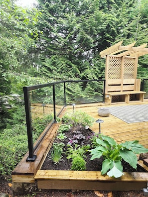 Eine Holzterrasse mit erhöhten Blumenbeeten, einer Holzpergola und einem Metallgeländer.