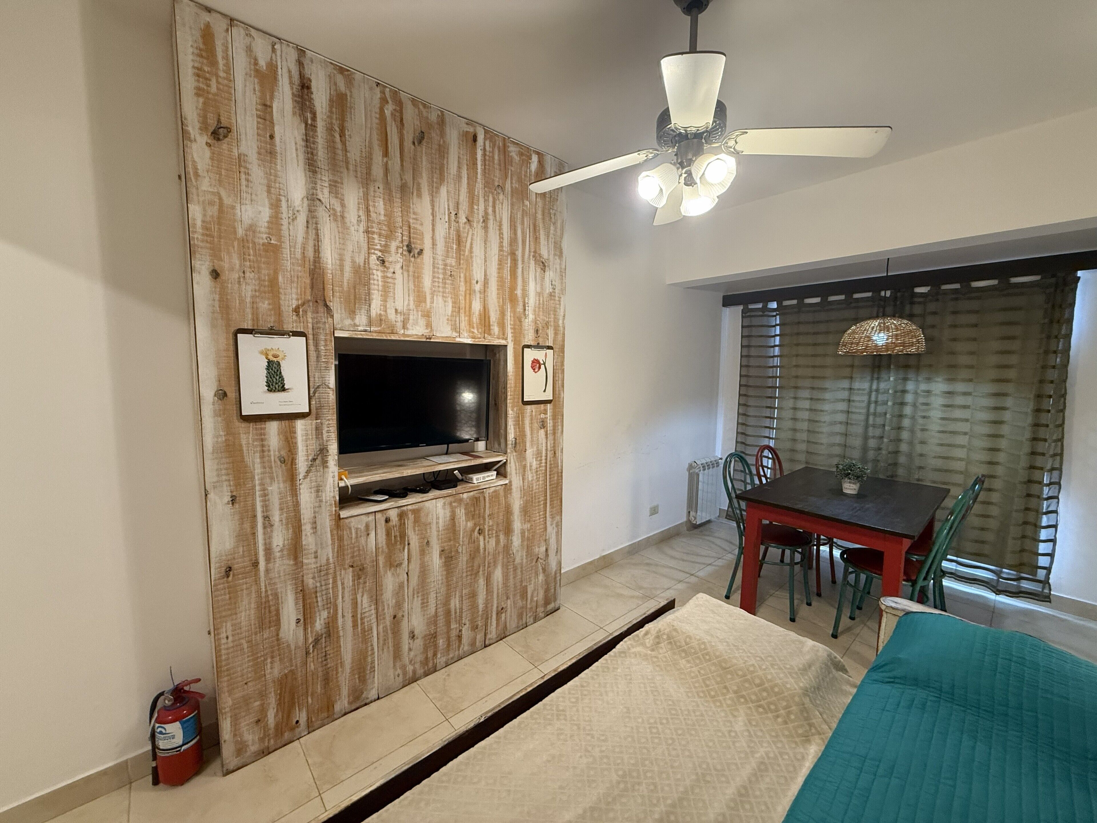 Ein Wohnzimmer mit einer Holzwandverkleidung, einem Deckenventilator, einem Esstisch mit Stühlen und einem großen Fenster mit Jalousien.