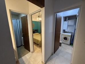 A hallway leading to a bedroom with a bed and a bathroom with a washing machine. - Comfortable Apartment Near Salta City Center (Salta)