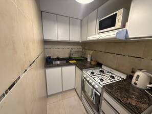 A compact kitchen with white cabinets, a gas stove, a microwave, and a sink. - Comfortable Apartment Near Salta City Center (Salta)