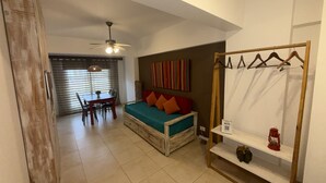 Ein gemütlicher Raum mit einem Bett, einem Esstisch, Stühlen, einem Deckenventilator und einem an der Wand befestigten Regal mit einer Laterne.