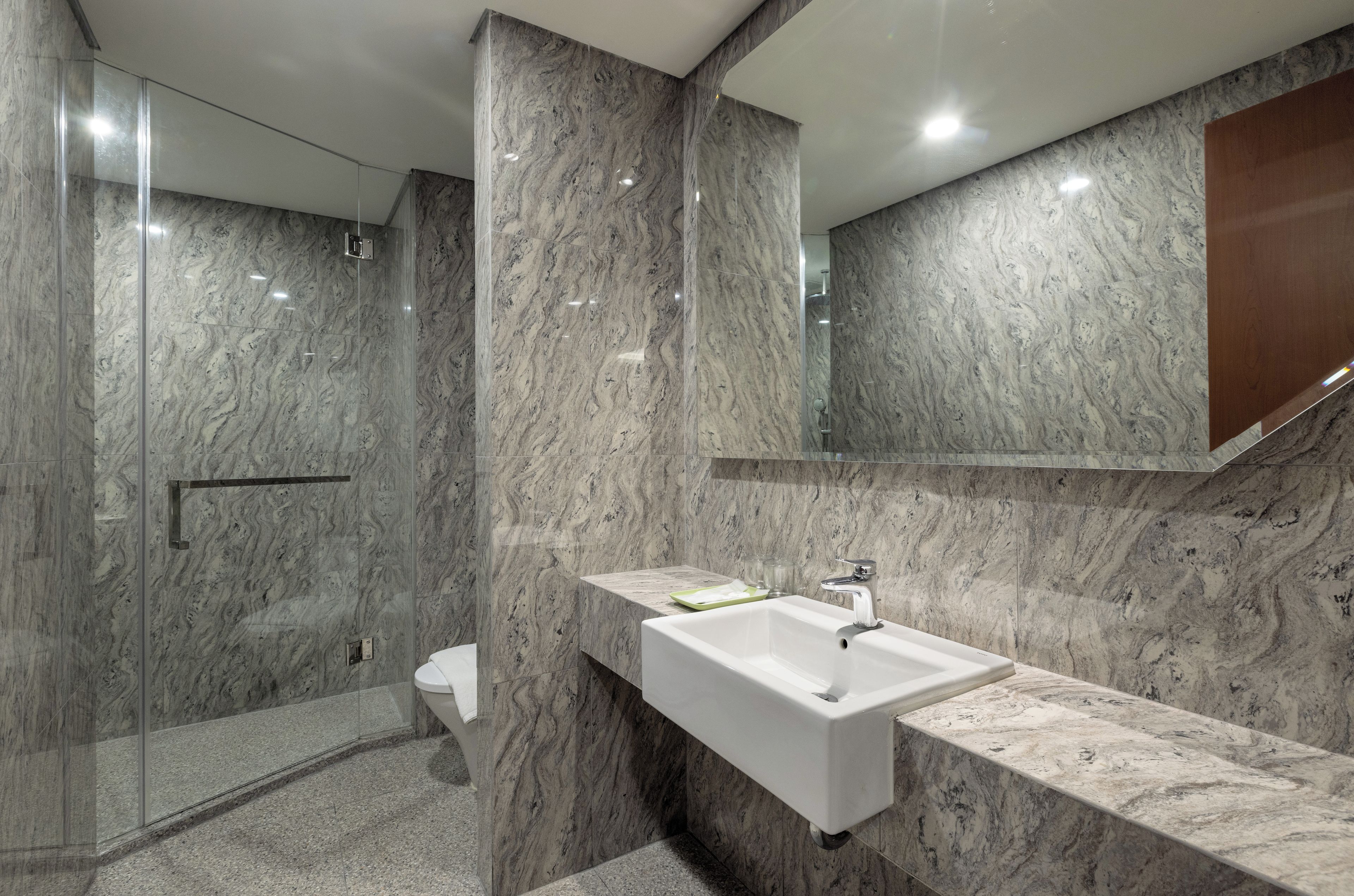 A modern bathroom with a marble wall, a glass shower enclosure, and a white sink with a mirror above it.