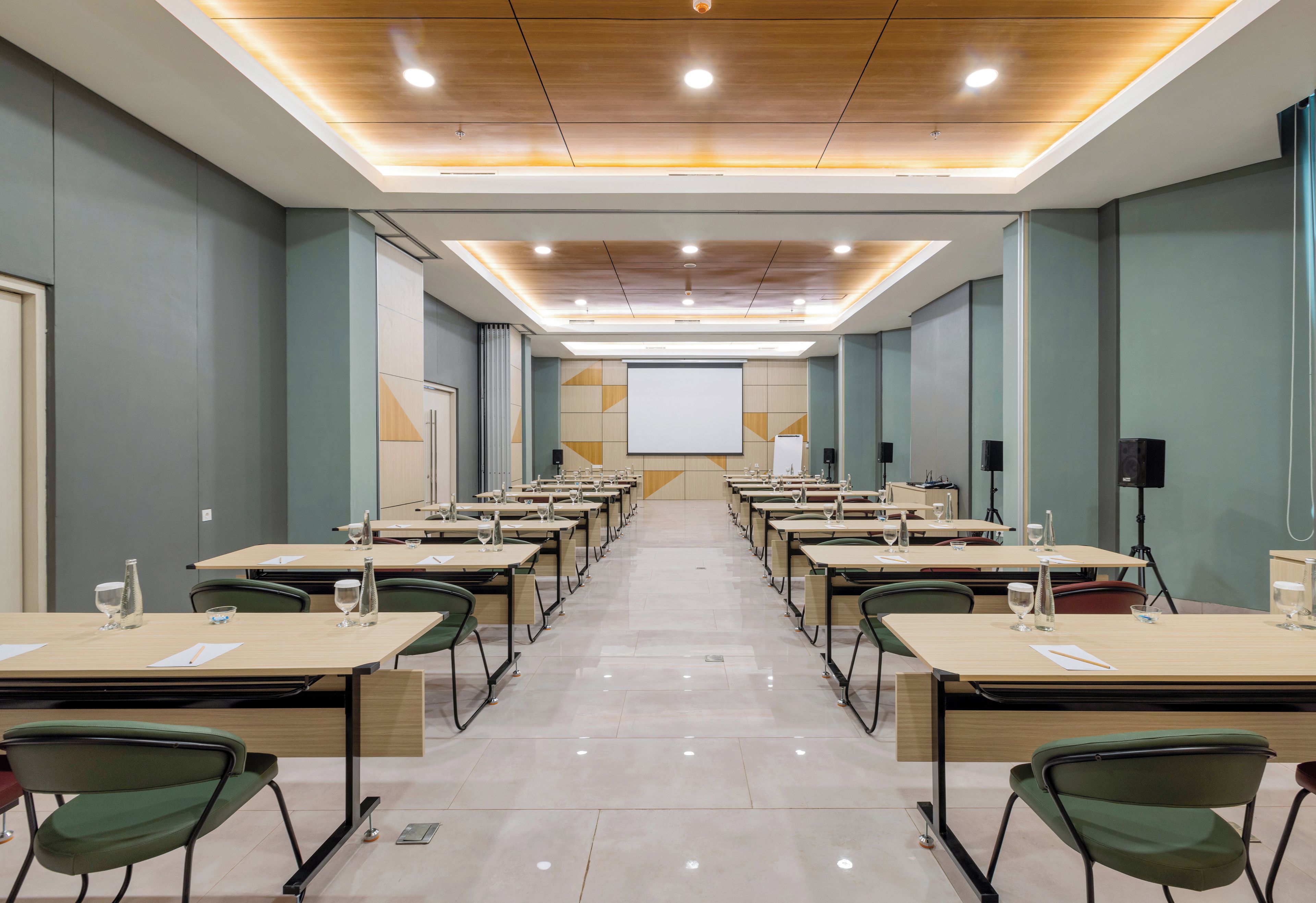 A conference room with a long table, chairs, a projector screen, and a presentation area.