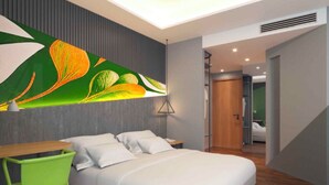 A modern hotel room with a bed, a desk, and a chair. There is a large window and a door leading to another room. - MAXONE Rota Wahid Hasyim (Jakarta)