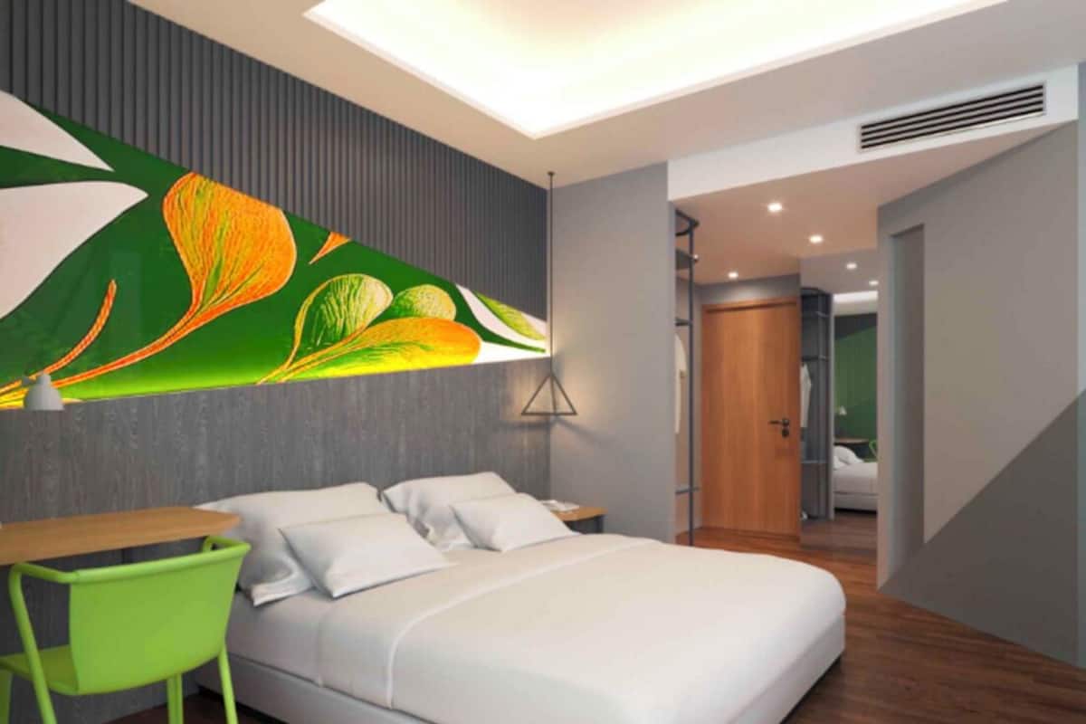 Una habitación de hotel moderna con una cama, un escritorio y una silla. Hay un ventanal grande y una puerta que da a otra habitación.