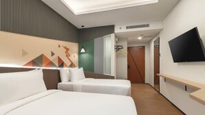 Habitación de hotel con cama, sofá, televisor montado en la pared y un pasillo que conduce a una puerta.