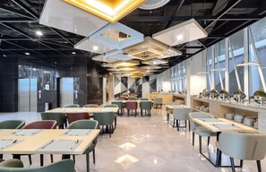 A modern restaurant interior with high ceilings, geometric light fixtures, and a buffet area. - MAXONE Rota Wahid Hasyim (Jakarta)