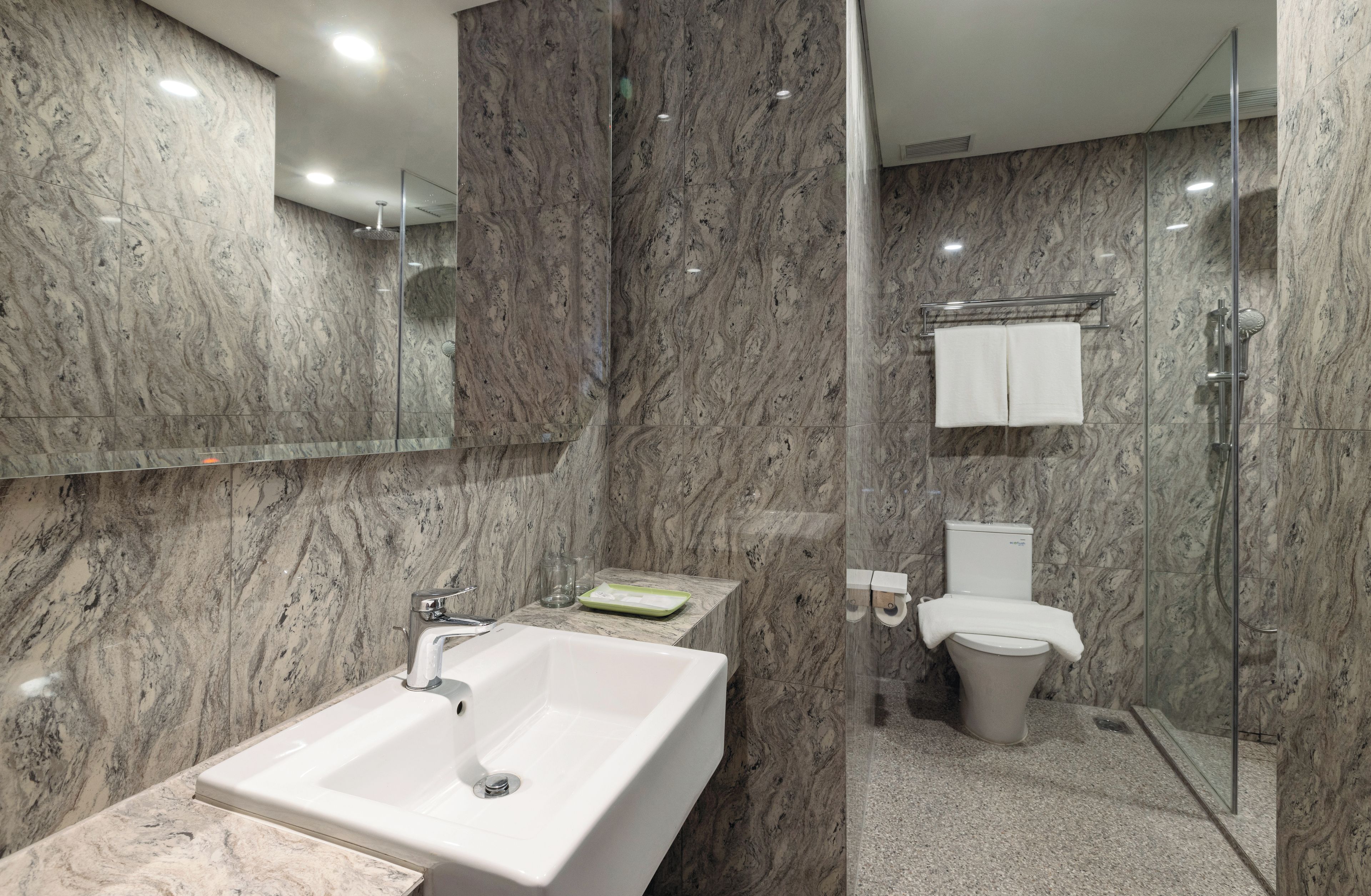 Ein modernes Badezimmer mit Marmorwand, einer Duschkabine aus Glas, einem weißen Waschbecken und einer Toilette.