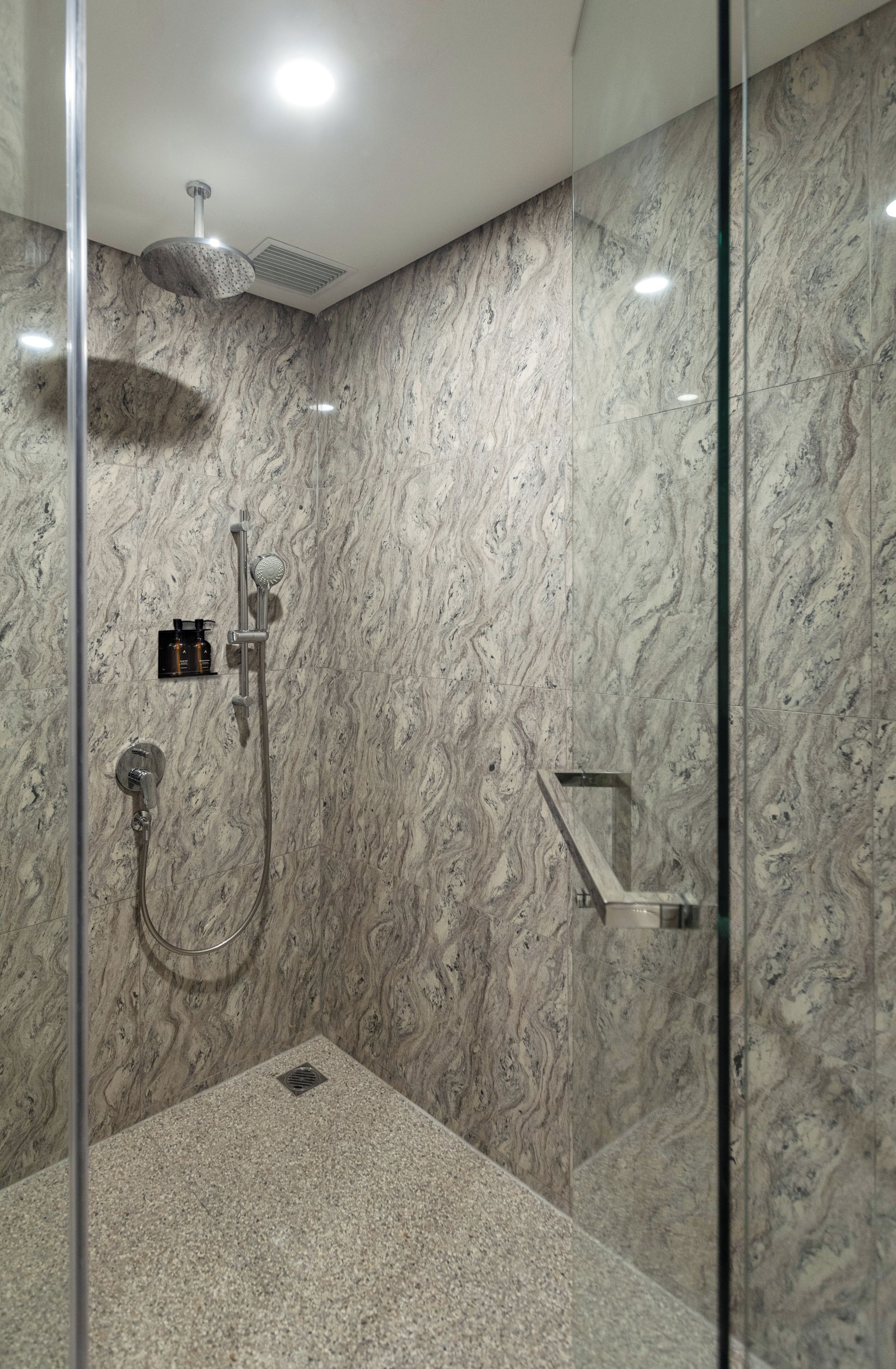 Una ducha moderna con cabina de vidrio, paredes de mármol y un cabezal de ducha manual.