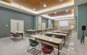 A conference room with multiple tables and chairs, a projector screen, and a speaker. - MAXONE Rota Wahid Hasyim (Jakarta)