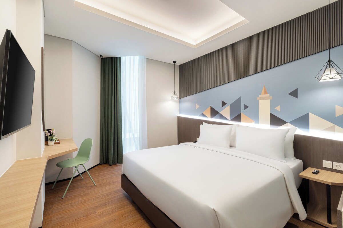 A modern hotel room with a bed, a desk, a chair, a TV, and a decorative wall.