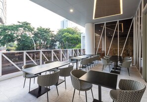 An outdoor cafe with tables and wicker chairs, overlooking a cityscape. - MAXONE Rota Wahid Hasyim (Jakarta)