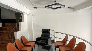 Una sala conferenze con un lungo tavolo e sei sedie, una scala e una parete bianca.