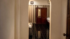 Un corridoio con uno specchio, una porta e vista su una stanza con un letto e un armadio.