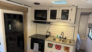 Een kleine keuken met een magnetron, fornuis, spoelbak en witte keukenkastjes.