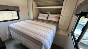 Een compact slaapkamer in een camper met een bed, een raam en een klein tafeltje.