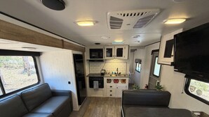 Een compact RV-interieur met een kitchenette, een zithoek en een aan de muur bevestigde televisie.