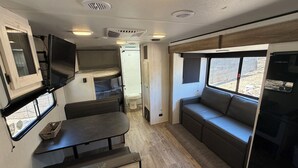 Een compact RV-interieur met een kitchenette, een zithoek, een klein tafeltje en een televisie.