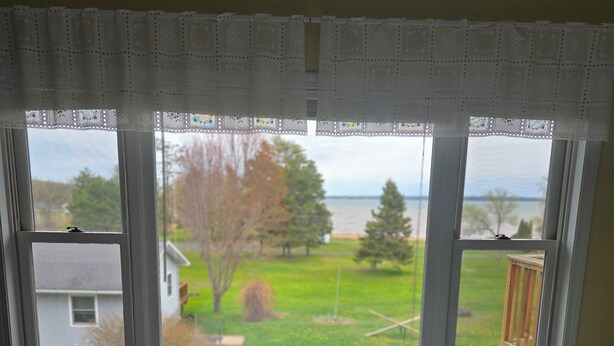Ein Schlafzimmer mit großem Fenster, einem Bett mit weißem Punkte-Bettbezug und Blick auf einen grünen Rasen und Bäume.