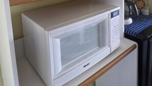 Eine weiße Mikrowelle auf einem Regal, Holzklinken an einem Schrank und eine Glastür mit einem Weinglas darin.