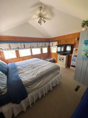 Ein Schlafzimmer mit einem Bett, einem Deckenventilator, einem Fernseher und einem Fenster mit Vorhängen.