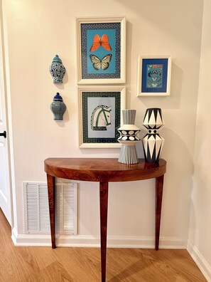 Un mur orné de tableaux encadrés, un vase décoratif et une table avec une lampe.