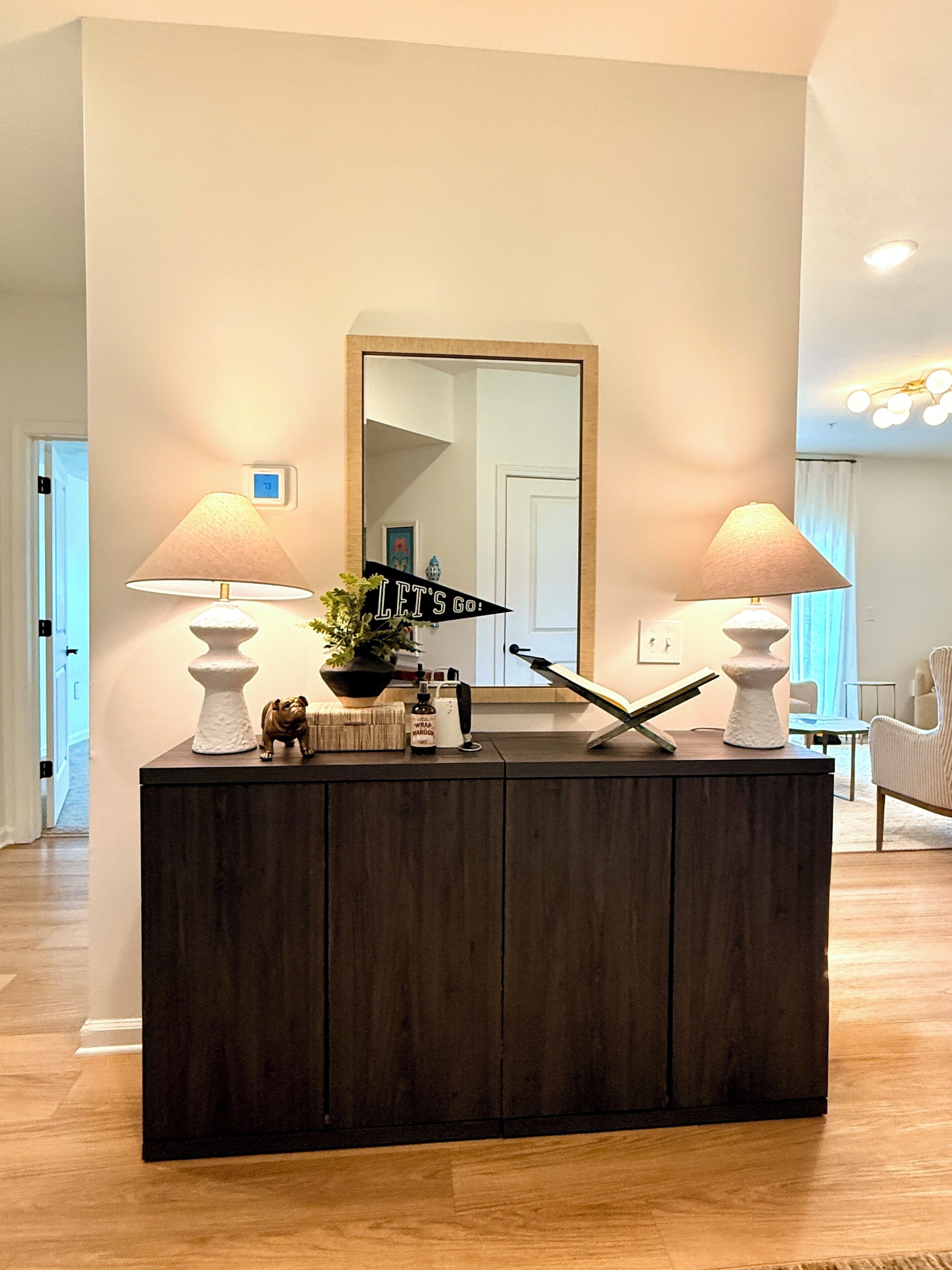 A dark wood console table with two lamps, a mirror, and decorative items.