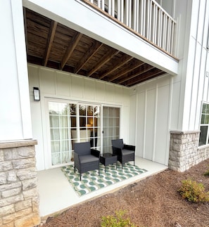 A covered patio with two chairs and a table, a stone wall, and a wooden ceiling. - StarkVilla - Walk to Davis Wade · 3BR/3.5BA (Starkville)