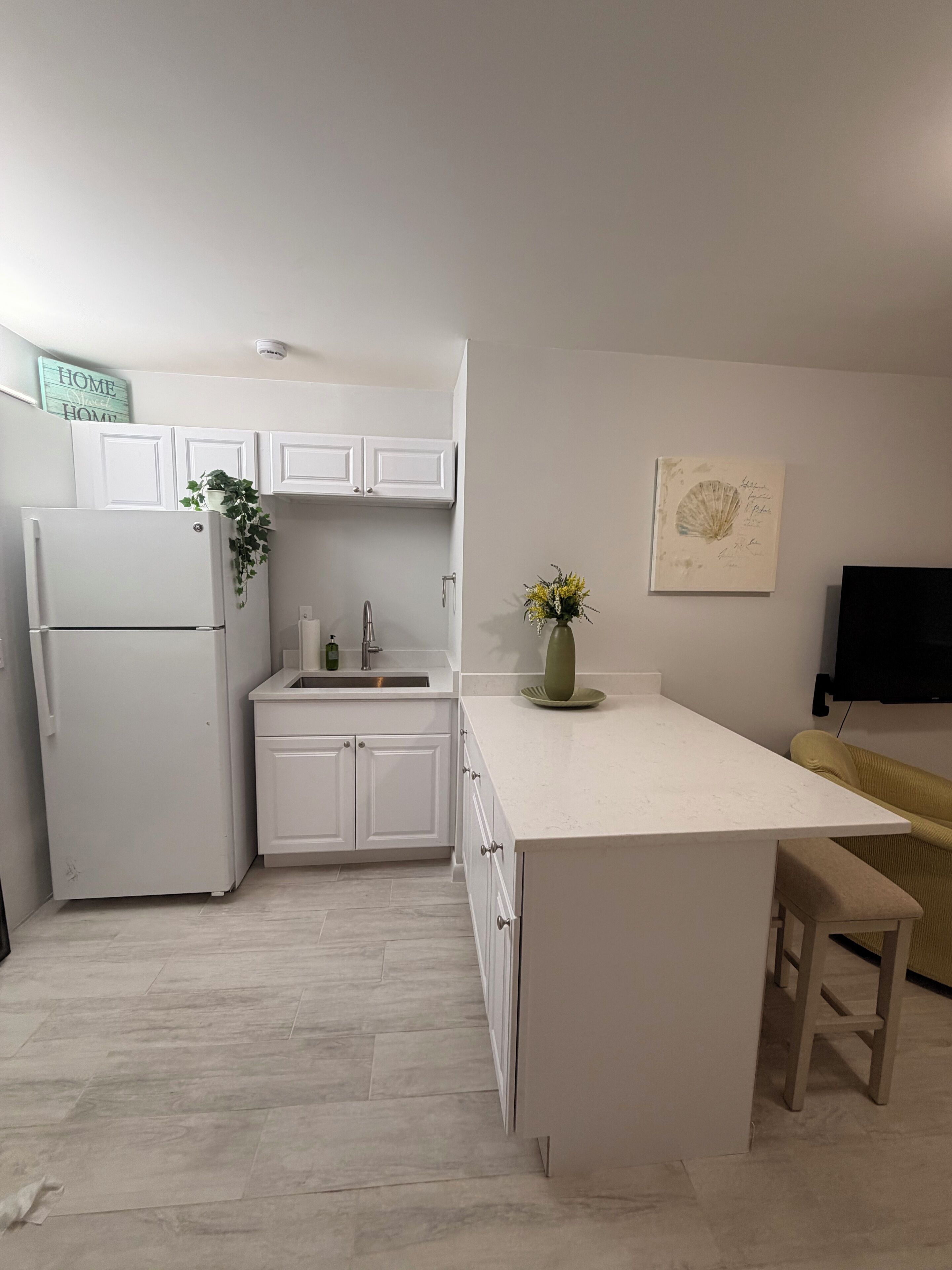 A modern kitchen with white cabinetry, a built-in refrigerator, a sink, and a small island with a bench.