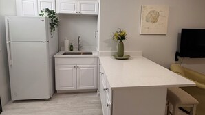A modern kitchen with white cabinetry, a built-in refrigerator, a sink, and a small island with a bench.