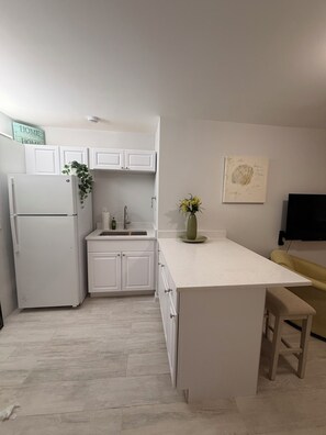 Eine moderne Küche mit weißen Schränken, einem eingebauten Kühlschrank, einer Spüle und einer kleinen Kochinsel mit Sitzbank.