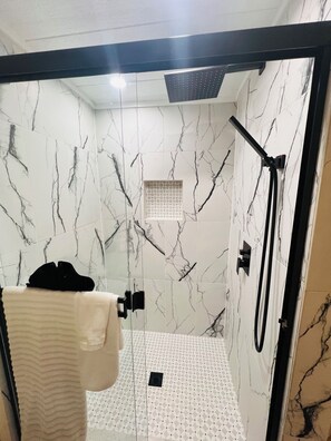 Une salle de bain moderne avec des murs en marbre, une douche en verre et un porte-serviettes.