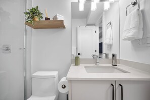 Ein modernes Badezimmer mit Toilette, Waschbecken, Spiegel und Ablagefläche mit Pflanze und Pflegeprodukten.